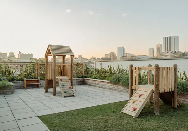 Dachspielplatz mit Holzklettergerüst, Rasenfläche und Blick auf die Skyline