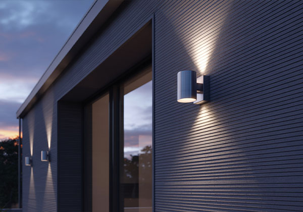Moderne Edelstahl-Fassadenleuchte an dunkler Hauswand in der Abenddämmerung