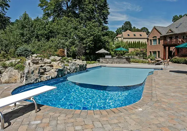 Pool mit Felsen und Sprungbrett, eingefasst von Naturstein und üppiger Bepflanzung