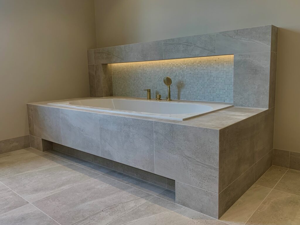 Badewanne mit Fliesenverkleidung, goldener Armatur und hinterleuchteter Nische