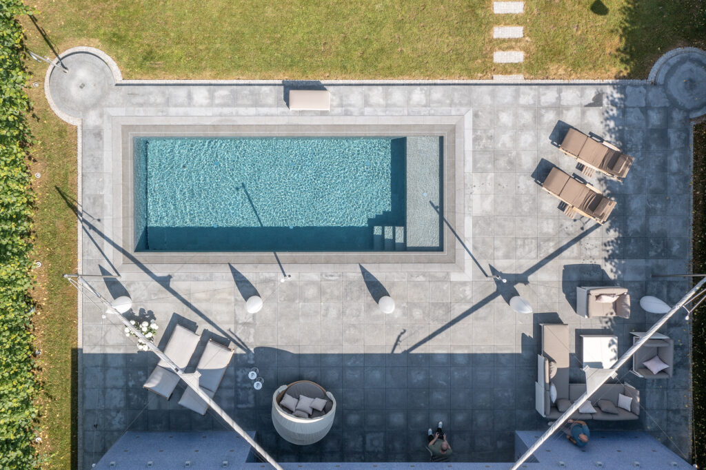 Luftaufnahme eines rechteckigen Pools mit umliegender Lounge und Rasenfläche