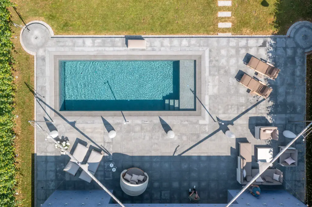 Luftaufnahme eines rechteckigen Pools mit umliegender Lounge und Rasenfläche