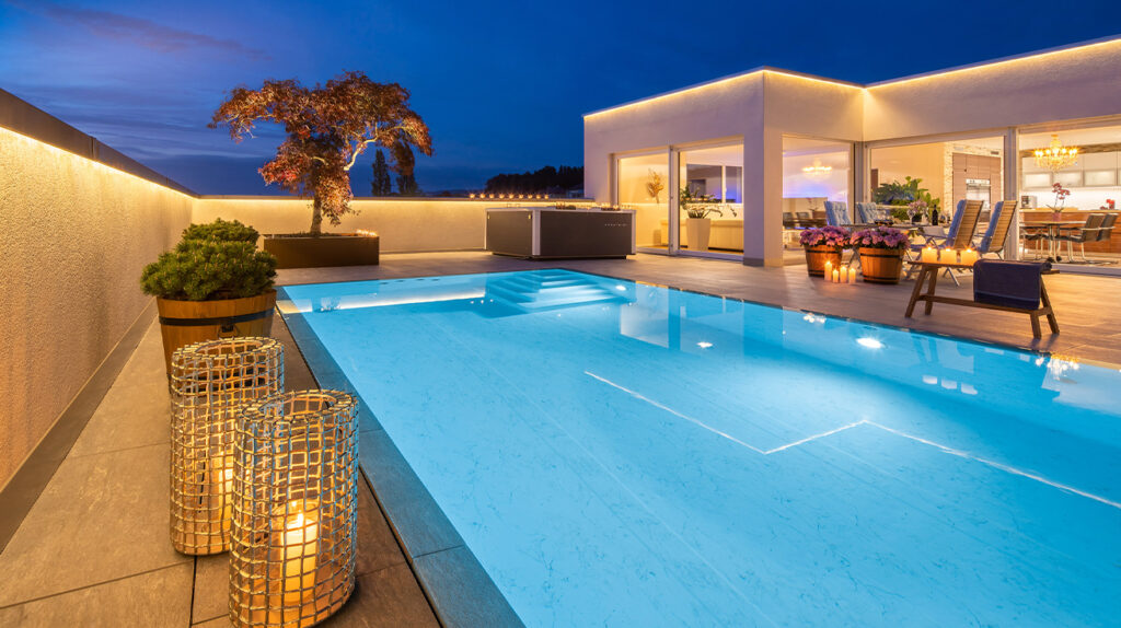 Moderner Dachgarten mit beleuchtetem Pool, Kübelpflanzen und stimmungsvoller Abendbeleuchtung