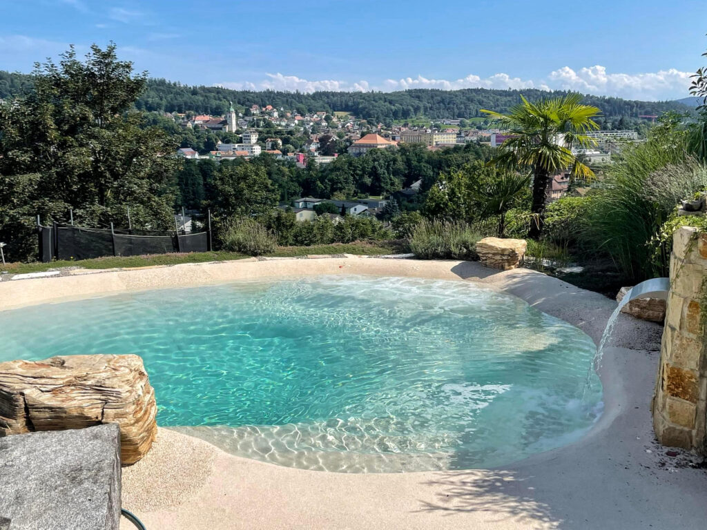Mediterraner Beachpool mit Wasserfall und Blick auf hügelige Landschaft mit Dorf