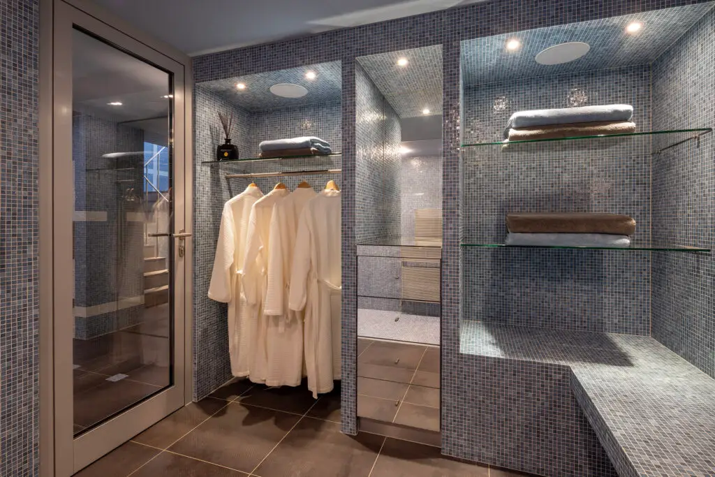 Umkleide mit Glasregalen, Bademänteln und blauen Mosaikfliesen