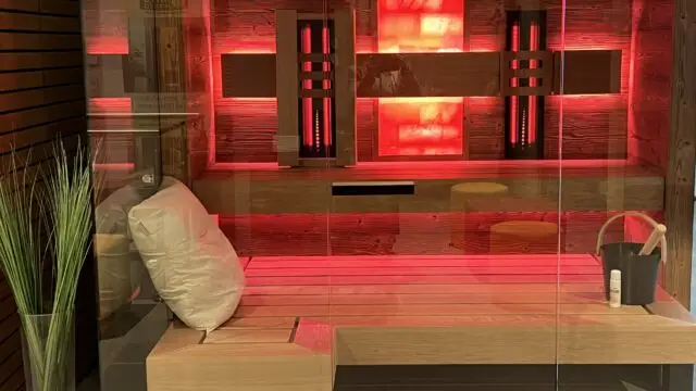 Moderne Sauna mit indirekter roter LED-Beleuchtung, beleuchteter Salzsteinwand, Liegebank und Saunaeimer.