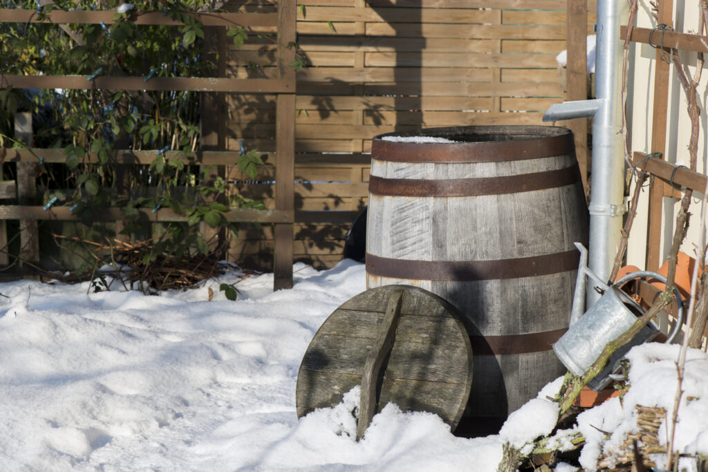 Verschneite Regentonne und Gartenzubehör im Wintergarten.